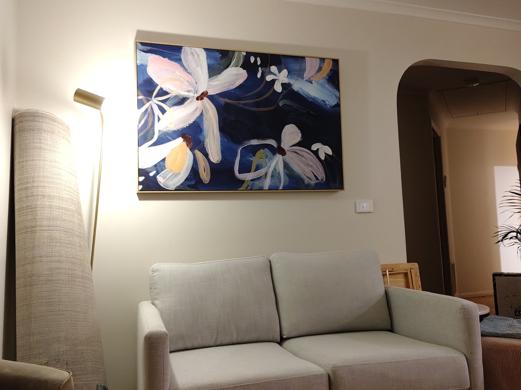 a photo of a bland couch with a bland painting. The painting is a loose sketch of flowers, but some of the petals are incomplete 